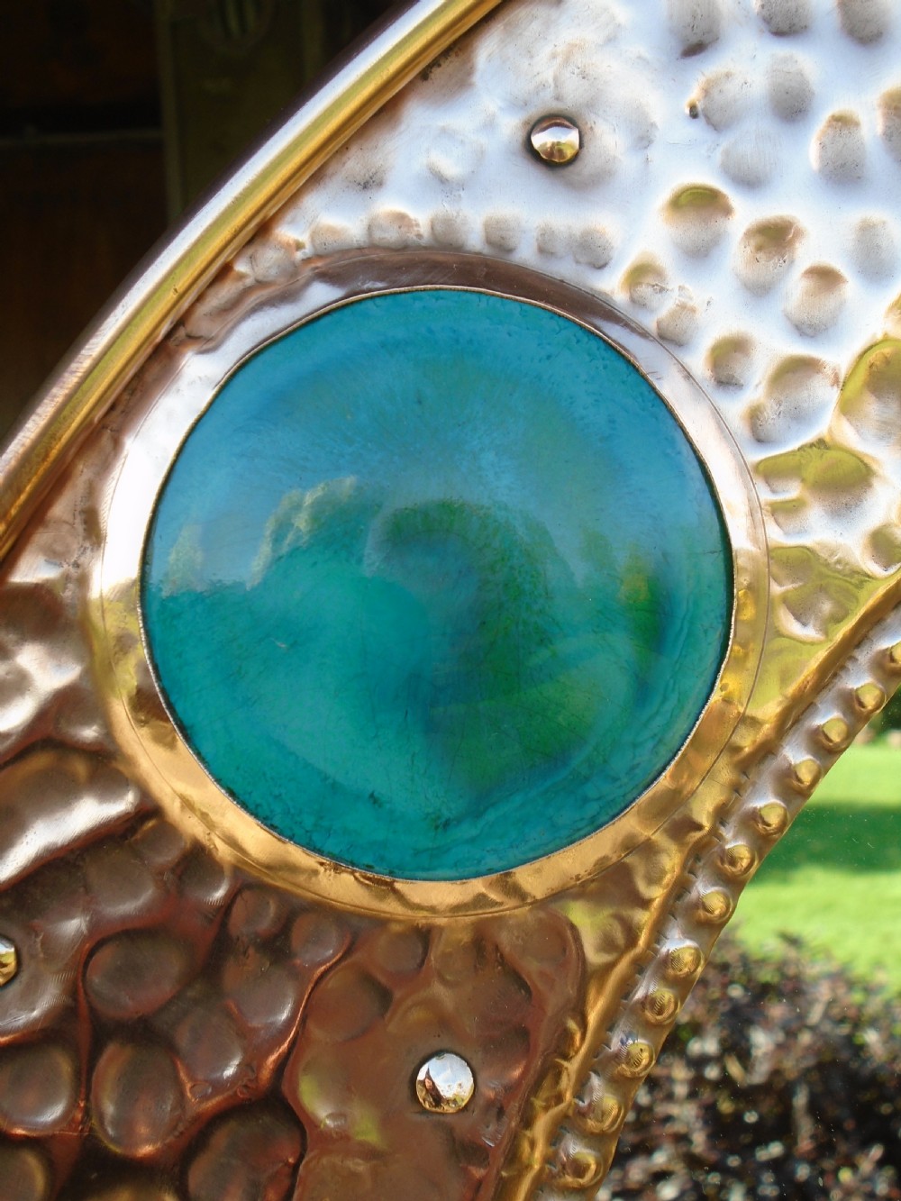 An oval Arts and Crafts wall mirror featuring a hand-hammered copper frame decorated with repousse floral motifs and four turquoise round cabochons. View IV