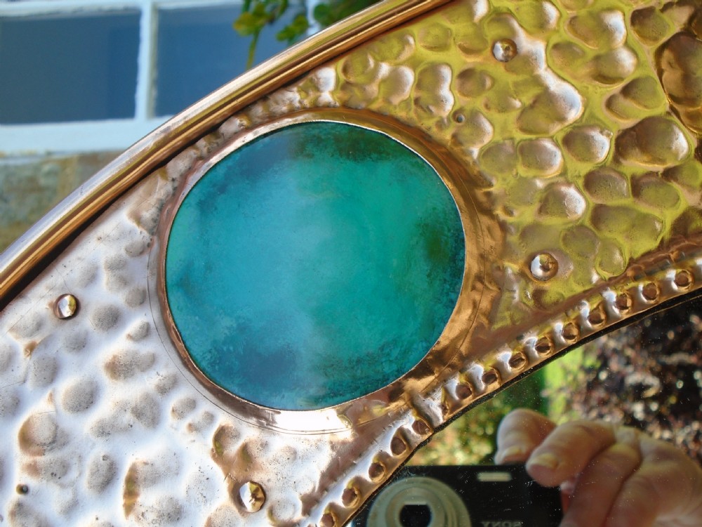 An oval Arts and Crafts wall mirror featuring a hand-hammered copper frame decorated with repousse floral motifs and four turquoise round cabochons. View VI