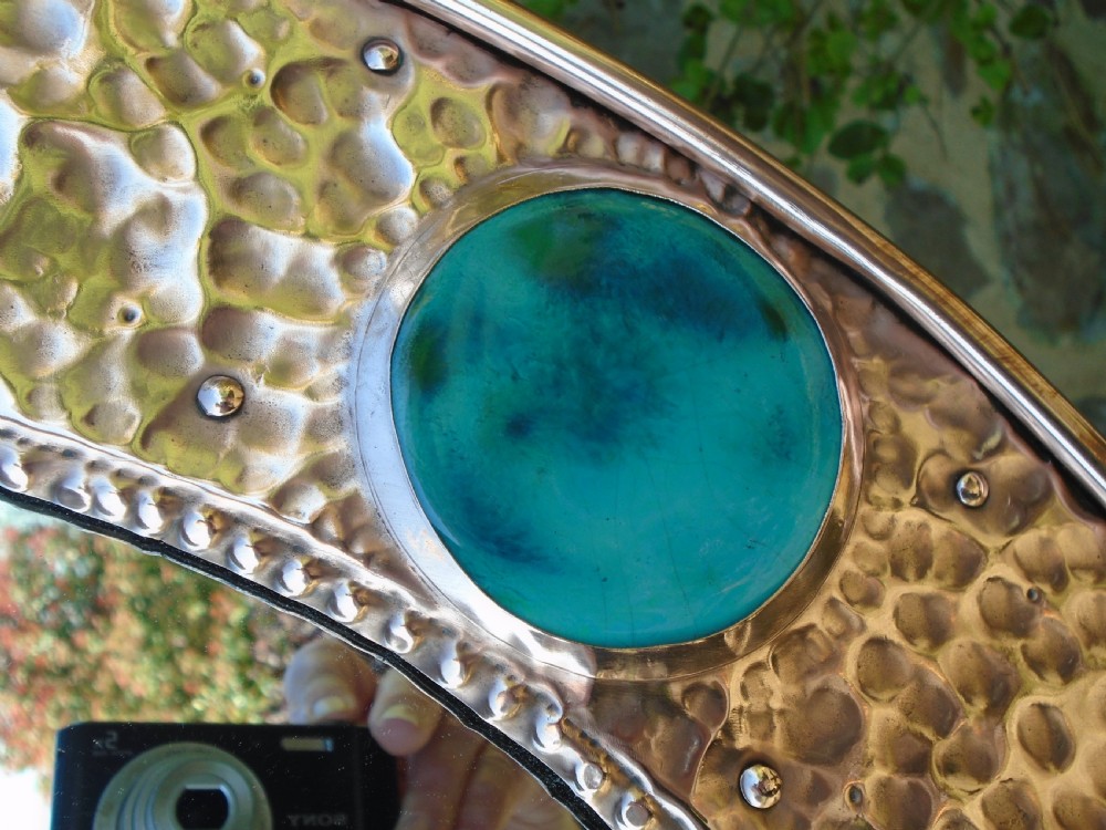 An oval Arts and Crafts wall mirror featuring a hand-hammered copper frame decorated with repousse floral motifs and four turquoise round cabochons. View VII