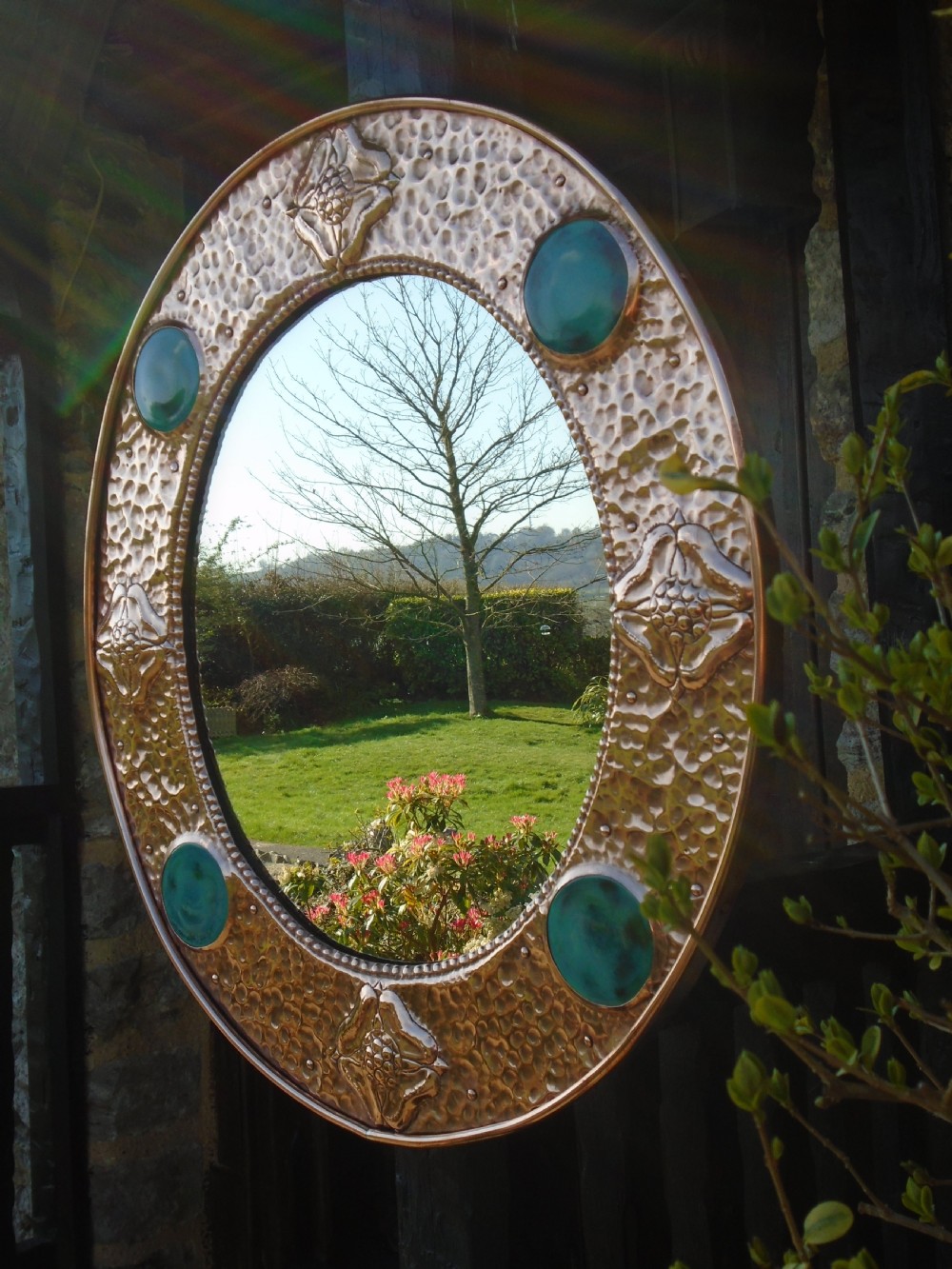 An oval Arts and Crafts wall mirror featuring a hand-hammered copper frame decorated with repousse floral motifs and four turquoise round cabochons. View IX