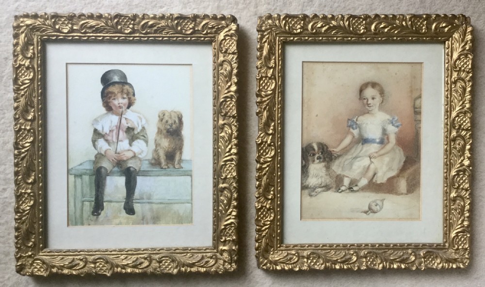 A pair of framed Victorian watercolour portraits depicting a boy and a girl seated with their respective dogs, set within elaborate carved gilt frames.