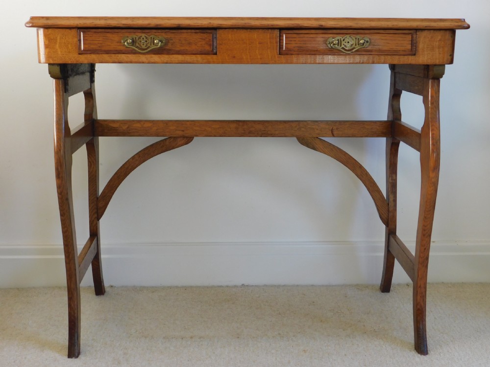A Victorian oak writing table featuring two drawers with brass drop handles and curved leg braces.