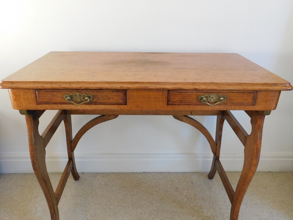 A Victorian oak writing table featuring two drawers with brass drop handles and curved leg braces. View V