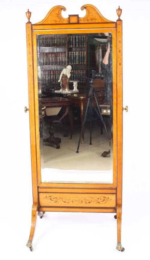 fig 1. An Edwardian satinwood cheval mirror featuring intricate marquetry inlay, an arched pediment with finials, side adjusters, and splayed legs with brass castors.