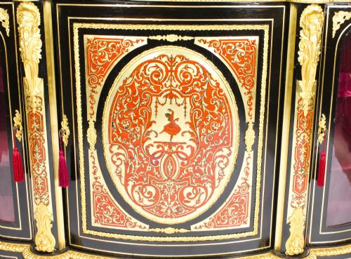 fig 9. A nineteenth-century ebonised serpentine credenza featuring brass and tortoiseshell Boulle marquetry, cast gilt-bronze ormolu mounts, a central panelled door, and glass display sides.