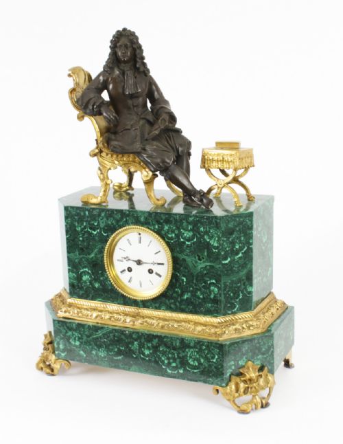 fig 1. A nineteenth-century French mantel clock featuring a green malachite base with gilt bronze mounts, a white enamel dial with Roman numerals, and a dark bronze figure seated on a gilt chair.
