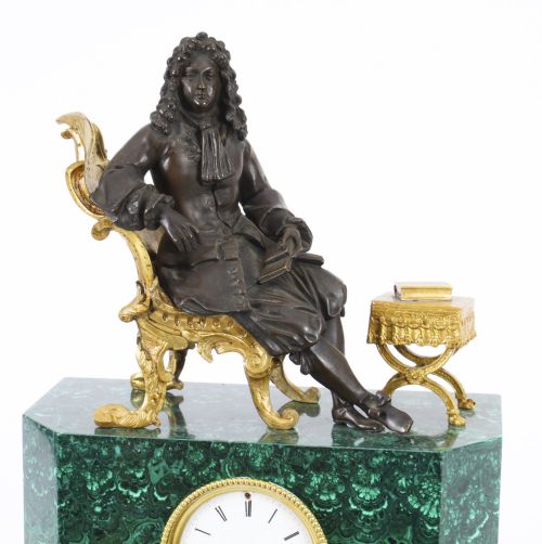 fig 2. A nineteenth-century French mantel clock featuring a green malachite base with gilt bronze mounts, a white enamel dial with Roman numerals, and a dark bronze figure seated on a gilt chair.