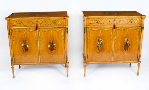 fig 1. A pair of 19th-century Adam Revival painted satinwood side cabinets featuring painted oval musical medallions, draped garlands, single top drawers, double cupboards, and turned tapered legs.