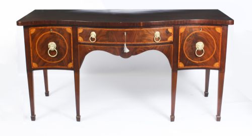 fig 1. An 18th-century George III flame mahogany serpentine sideboard featuring inlaid circular panel doors, brass lion-mask ring handles, and tapered square legs terminating in spade feet.