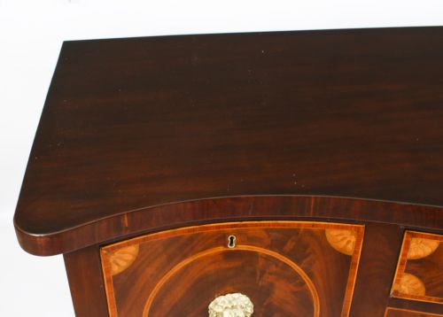 fig 2. An 18th-century George III flame mahogany serpentine sideboard featuring inlaid circular panel doors, brass lion-mask ring handles, and tapered square legs terminating in spade feet.