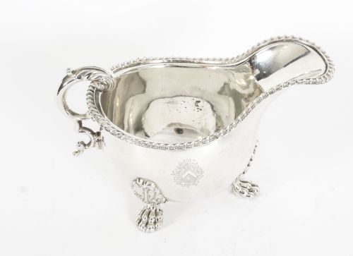 fig 1. A pair of 19th-century silver-plated sauce boats featuring scroll handles, engraved crests, and claw feet against a white background.
