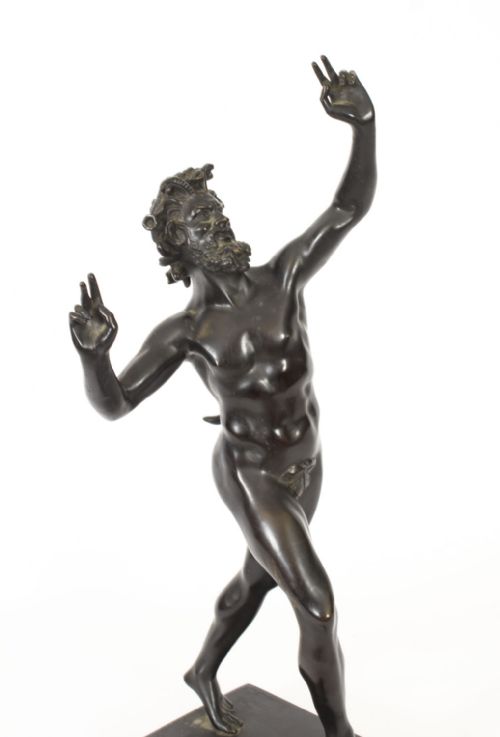 fig 2. A dark patinated bronze figure depicting a dancing faun with raised hands standing on a stepped rectangular base.
