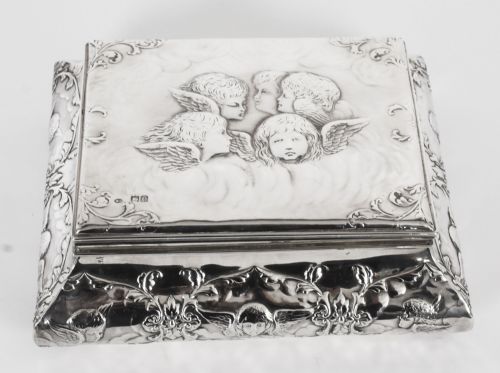 fig 1. A rectangular sterling silver casket featuring relief repousse cherub heads on the hinged lid and scrollwork along the flared base.