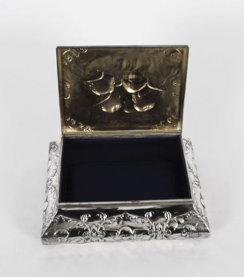 fig 3. A rectangular sterling silver casket featuring relief repousse cherub heads on the hinged lid and scrollwork along the flared base.