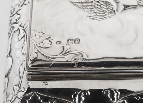 fig 5. A rectangular sterling silver casket featuring relief repousse cherub heads on the hinged lid and scrollwork along the flared base.