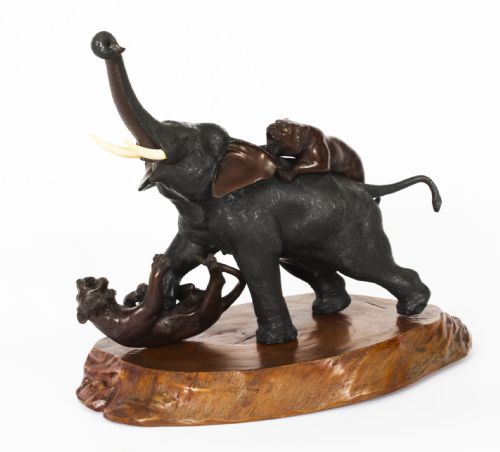 fig 1. A dark patinated bronze sculpture of an elephant defending against two tigers, mounted on a polished natural wood base.