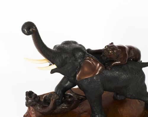 fig 2. A dark patinated bronze sculpture of an elephant defending against two tigers, mounted on a polished natural wood base.