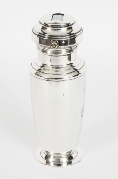 fig 3. An Art Deco silver plated cocktail shaker featuring an engraved monogram letter D and a top section with a recipe viewing window.