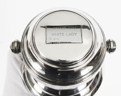fig 4. An Art Deco silver plated cocktail shaker featuring an engraved monogram letter D and a top section with a recipe viewing window.