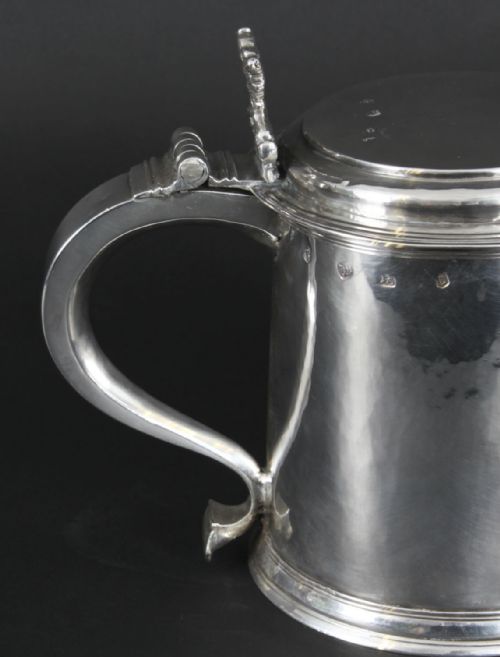fig 2. A seventeenth-century sterling silver lidded tankard featuring a tapered cylindrical body, a scroll handle with a hinged thumbpiece, and visible hallmarks.