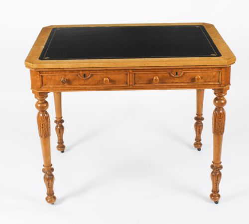 fig 1. A late 19th-century birdseye maple writing table featuring a black leather inset top, two front frieze drawers, and turned carved legs on brass castors.