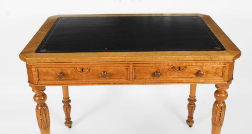 fig 5. A late 19th-century birdseye maple writing table featuring a black leather inset top, two front frieze drawers, and turned carved legs on brass castors.