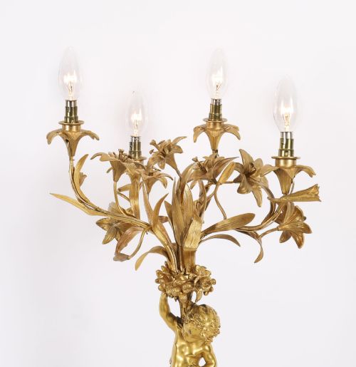 fig 1. A French gilt bronze table lamp featuring a sculpted cherub holding lily-shaped light sockets on a Rococo scrolled base.
