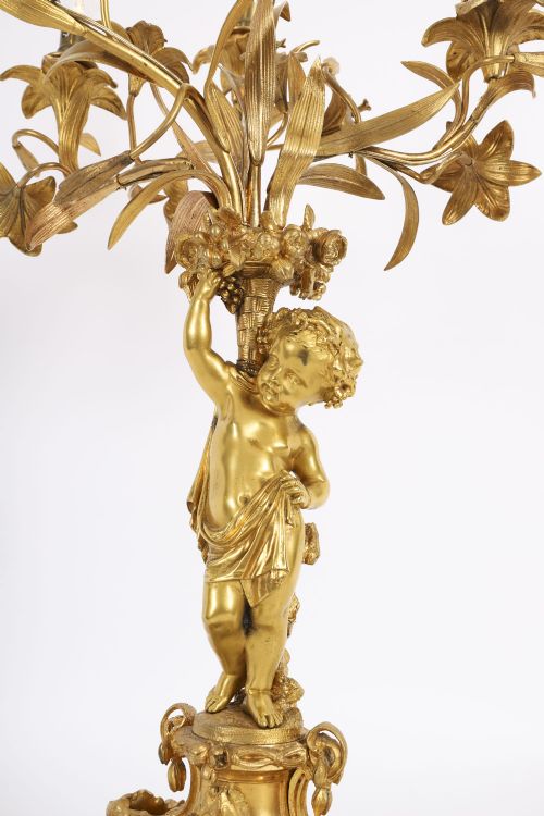 fig 2. A French gilt bronze table lamp featuring a sculpted cherub holding lily-shaped light sockets on a Rococo scrolled base.