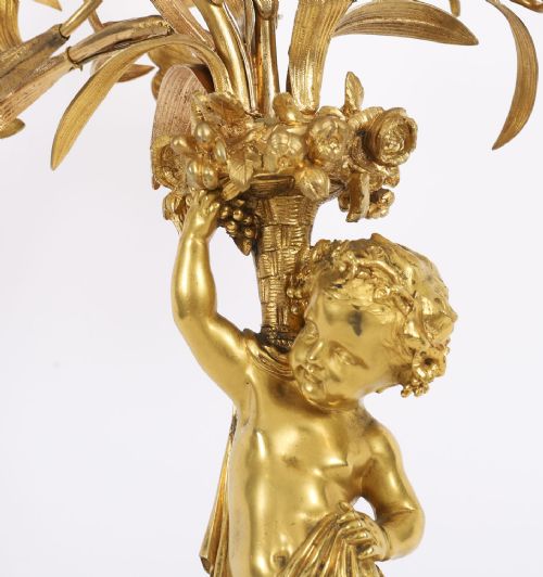 fig 4. A French gilt bronze table lamp featuring a sculpted cherub holding lily-shaped light sockets on a Rococo scrolled base.