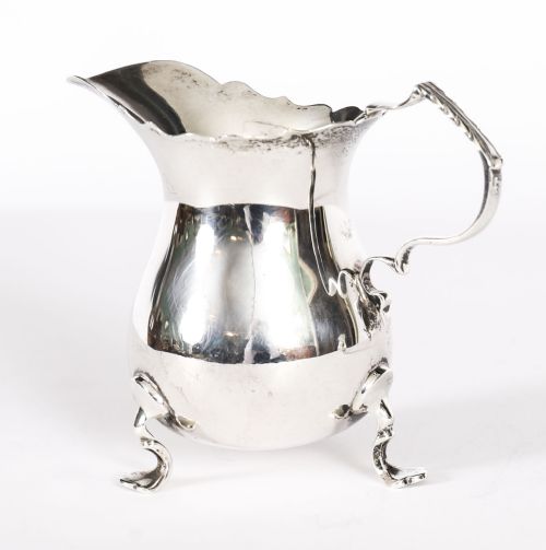 fig 1. A graduating pair of Victorian sterling silver cream jugs featuring scalloped rims, scroll handles, and tripod legs.