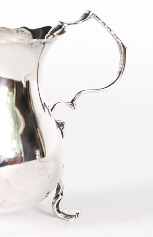 fig 2. A graduating pair of Victorian sterling silver cream jugs featuring scalloped rims, scroll handles, and tripod legs.