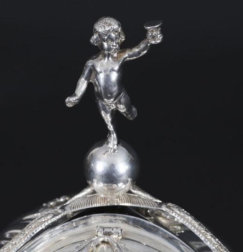 fig 2. An antique silver-plated folding biscuit box featuring scalloped shell compartments, a top cherub finial, and decorative figurative side supports.