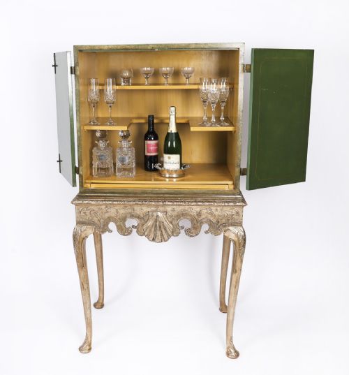 fig 1. A green lacquered two-door cocktail cabinet with hand-painted chinoiserie scenes resting on a carved silver gilt stand with cabriole legs.