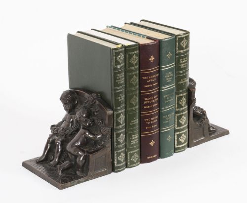 fig 1. A pair of dark brown patinated bronze bookends depicting seated classical cherubs holding floral garlands on stepped bases.