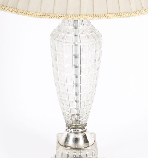 fig 3. An Art Deco table lamp featuring a faceted clear cut crystal stem, a square metal pedestal base, and a cream pleated fabric lampshade.