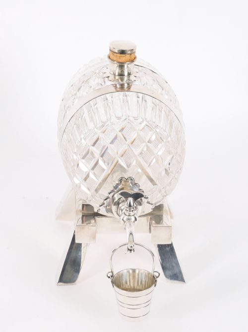 fig 3. A nineteenth-century cut crystal barrel decanter with silver-plated hoops, tap, and miniature bucket accessory resting on a four-legged silver stand.