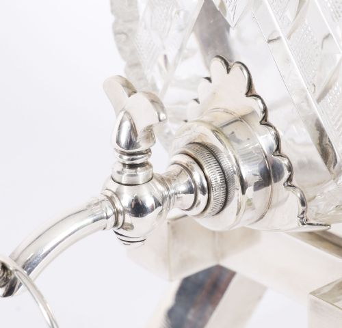 fig 4. A nineteenth-century cut crystal barrel decanter with silver-plated hoops, tap, and miniature bucket accessory resting on a four-legged silver stand.