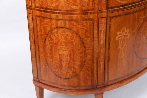 fig 5. A semicircular antique satinwood demilune cabinet featuring urn and swag marquetry inlays, a top drawer with a blue tassel key, and slender tapered legs.