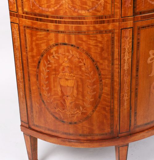 fig 8. A semicircular antique satinwood demilune cabinet featuring urn and swag marquetry inlays, a top drawer with a blue tassel key, and slender tapered legs.