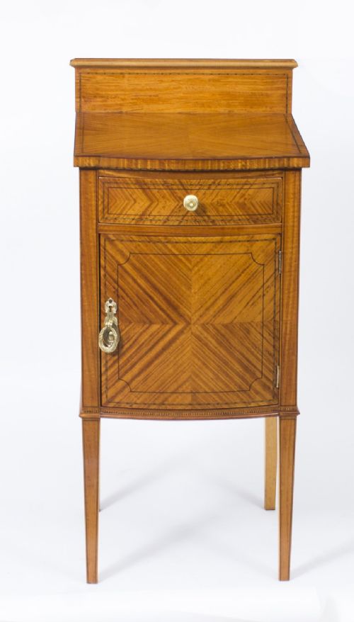 fig 3. A Victorian satinwood bedside cabinet featuring a bowfront shape, chevron veneer patterns, a single drawer, a cupboard door, and tapered square legs.