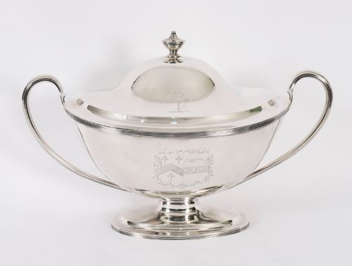 fig 1. A George III sterling silver tureen with two looped handles, a domed lid, a pedestal base, and an engraved heraldic crest.