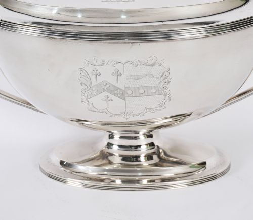 fig 5. A George III sterling silver tureen with two looped handles, a domed lid, a pedestal base, and an engraved heraldic crest.