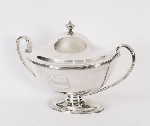 fig 7. A George III sterling silver tureen with two looped handles, a domed lid, a pedestal base, and an engraved heraldic crest.