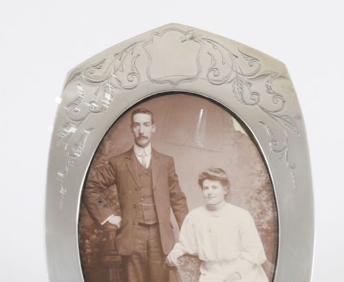 fig 1. An arched sterling silver photo frame featuring engraved floral motifs around an oval picture aperture.