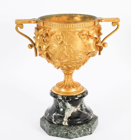 fig 1. A pair of nineteenth-century French gilt bronze classical urns featuring relief carvings and scroll handles, mounted on dark green marble bases.