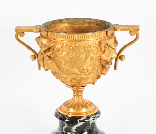 fig 6. A pair of nineteenth-century French gilt bronze classical urns featuring relief carvings and scroll handles, mounted on dark green marble bases.