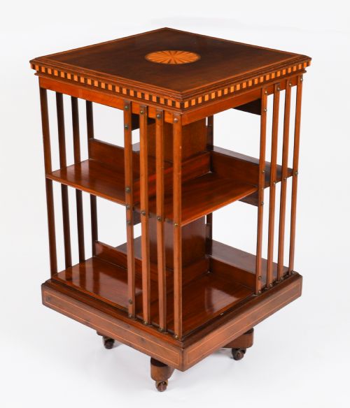 fig 3. An Edwardian flame mahogany revolving bookcase featuring two tiers, vertical slatted sides with brass studs, satinwood inlay, and castors.