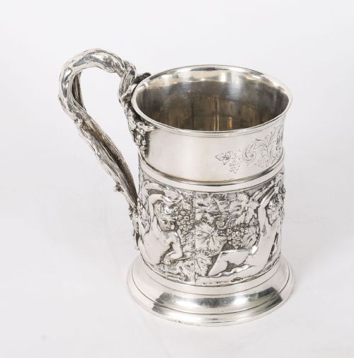 fig 1. A Victorian silver-plated mug featuring embossed putti and grapevine motifs, an engraved rim, a pint capacity mark, and a naturalistic branch-shaped handle.