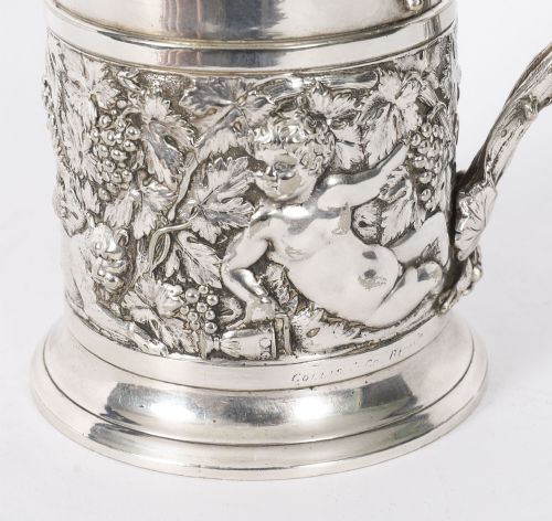 fig 2. A Victorian silver-plated mug featuring embossed putti and grapevine motifs, an engraved rim, a pint capacity mark, and a naturalistic branch-shaped handle.