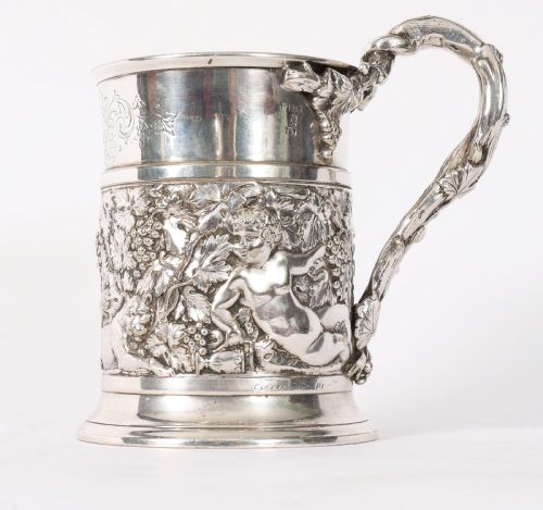 fig 3. A Victorian silver-plated mug featuring embossed putti and grapevine motifs, an engraved rim, a pint capacity mark, and a naturalistic branch-shaped handle.